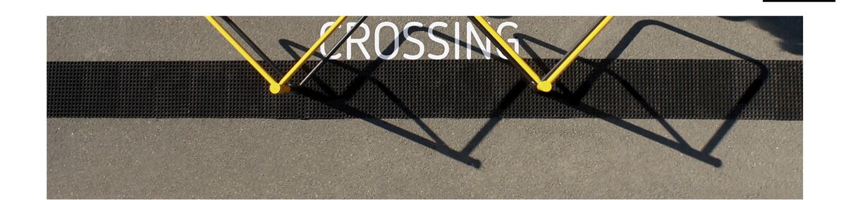 Yellow modular crossing gates casting shadows that read CROSSING
